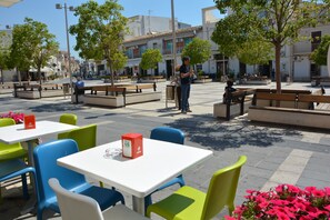 Un área de café al aire libre con mesas, sillas, bancos y plantas en macetas.