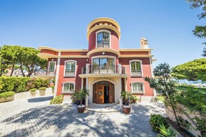 A large, multi-story building with a prominent central tower, multiple balconies, and a paved entrance area with potted plants. - Vila Santa Eulália (Albufeira)