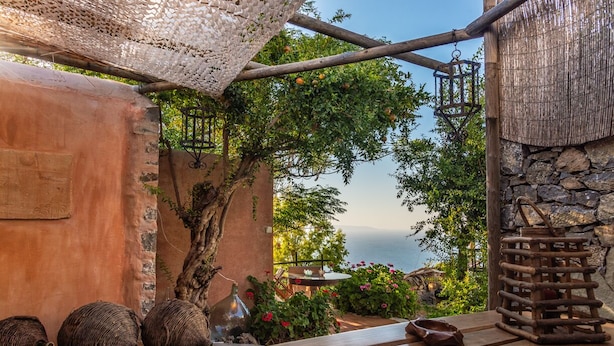 A rustic outdoor seating area with a wooden table, wicker baskets, and a stone wall. - The Old Pomegranate House - Sea view - AC - WIFI (Mirsini)