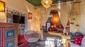 A cozy living room with a stone wall, a television, a wicker chair, and a sofa with red cushions. - The Old Pomegranate House - Sea view - AC - WIFI (Mirsini)