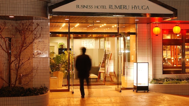 La entrada del Hotel Business Rumieru Hyuga, con una puerta de cristal, un cartel y una planta en maceta.