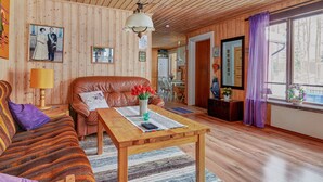 A cozy living room with a wooden ceiling, a leather sofa, a wooden coffee table, and a large window with purple curtains. - Lillarmsjö-cottage, cottage with lake view. (Lillarmsjö)