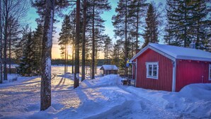 A red cabin with a snow-covered roof, surrounded by tall pine trees and a clear sky. - Lillarmsjö-cottage, cottage with lake view. (Lillarmsjö)
