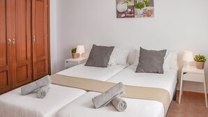 A hotel room with two beds, a wooden wardrobe, a wall-mounted artwork, and bedside tables with lamps and plants.