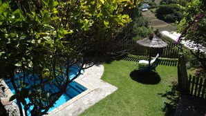 Un jardin avec une piscine, deux chaises longues, un chemin de pierres et une clôture en bois.