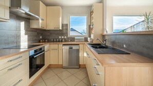 A modern kitchen with a dishwasher, oven, and a window overlooking a residential area. - Heated, well-equipped house/pool between Lacs d'Annecy and Aix-les-Bains (Rumilly)