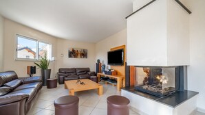 A modern living room with a leather sofa, a coffee table, two ottomans, a flat-screen TV, a fireplace, and a cityscape painting on the wall. - Heated, well-equipped house/pool between Lacs d'Annecy and Aix-les-Bains (Rumilly)