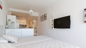 Ein Schlafzimmer mit einem großen Bett, einem an der Wand montierten Fernseher und einer Küchenzeile im Hintergrund.