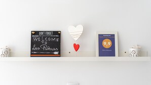 Eine Wand mit einem Regal, das ein Kreidetafel-Schild, eine gerahmte Auszeichnung und eine herzförmige Dekoration zeigt.