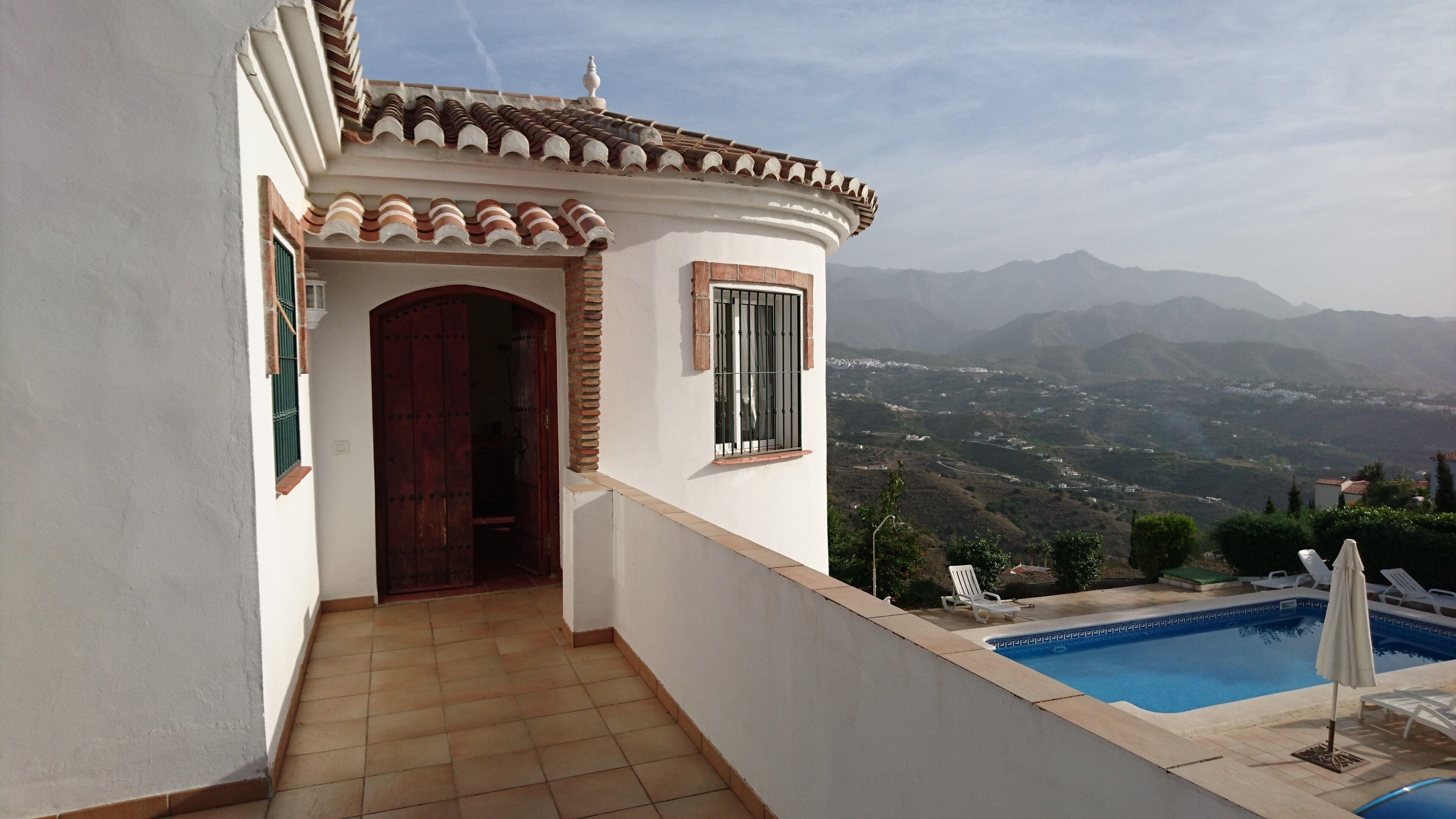 A balcony with a pool, a wooden door, and a view of mountains.