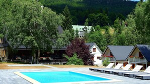 A swimming pool with lounge chairs, surrounded by trees and a mountain backdrop.