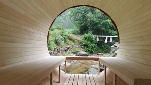 A wooden interior with a view of a natural landscape through an arched window, including a stream and greenery.