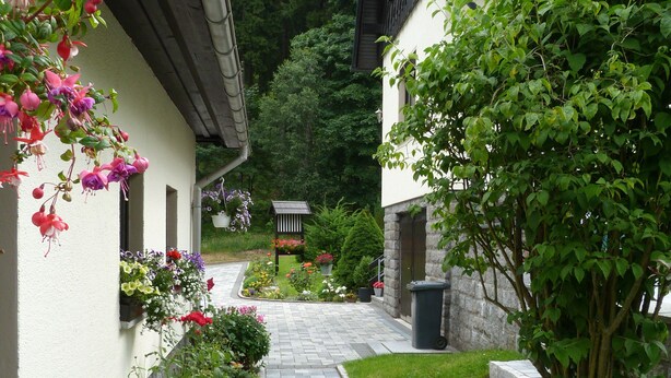 Un sendero que lleva a un edificio con fachada de piedra y un jardín con flores y arbustos.