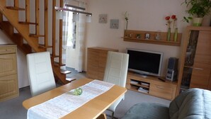 Una sala de estar con una mesa de madera, dos sillas, un sofá, un televisor y una escalera.