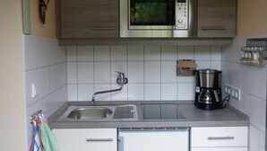 Una cocina con microondas de acero inoxidable, cafetera y lavabo con grifo.
