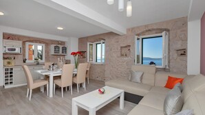 A modern living room with a beige sofa, a white coffee table, and a dining area with a white table and chairs. - NEW! Stone house in quiet location, heated pool + sea views, ideal for familys (Zivogosce)