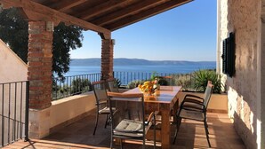 A covered patio with a table and chairs, overlooking a body of water and distant hills. - NEW! Stone house in quiet location, heated pool + sea views, ideal for familys (Zivogosce)