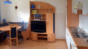 Ein gemütlicher Wohnbereich mit Küchenzeile, einem Essbereich mit rundem Tisch und Stühlen sowie einer integrierten Unterhaltungseinheit mit Fernseher.