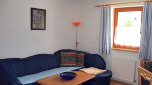 Ein Wohnzimmer mit einem dunkelblauen Sofa, einem Holztisch mit einer blauen Schale, einem gemusterten Kissen, einer Stehlampe und einem Fenster mit Vorhängen.
