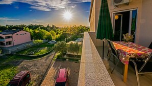 Un balcon avec une table et des chaises, donnant sur un quartier résidentiel avec un immeuble rose et des voitures garées.