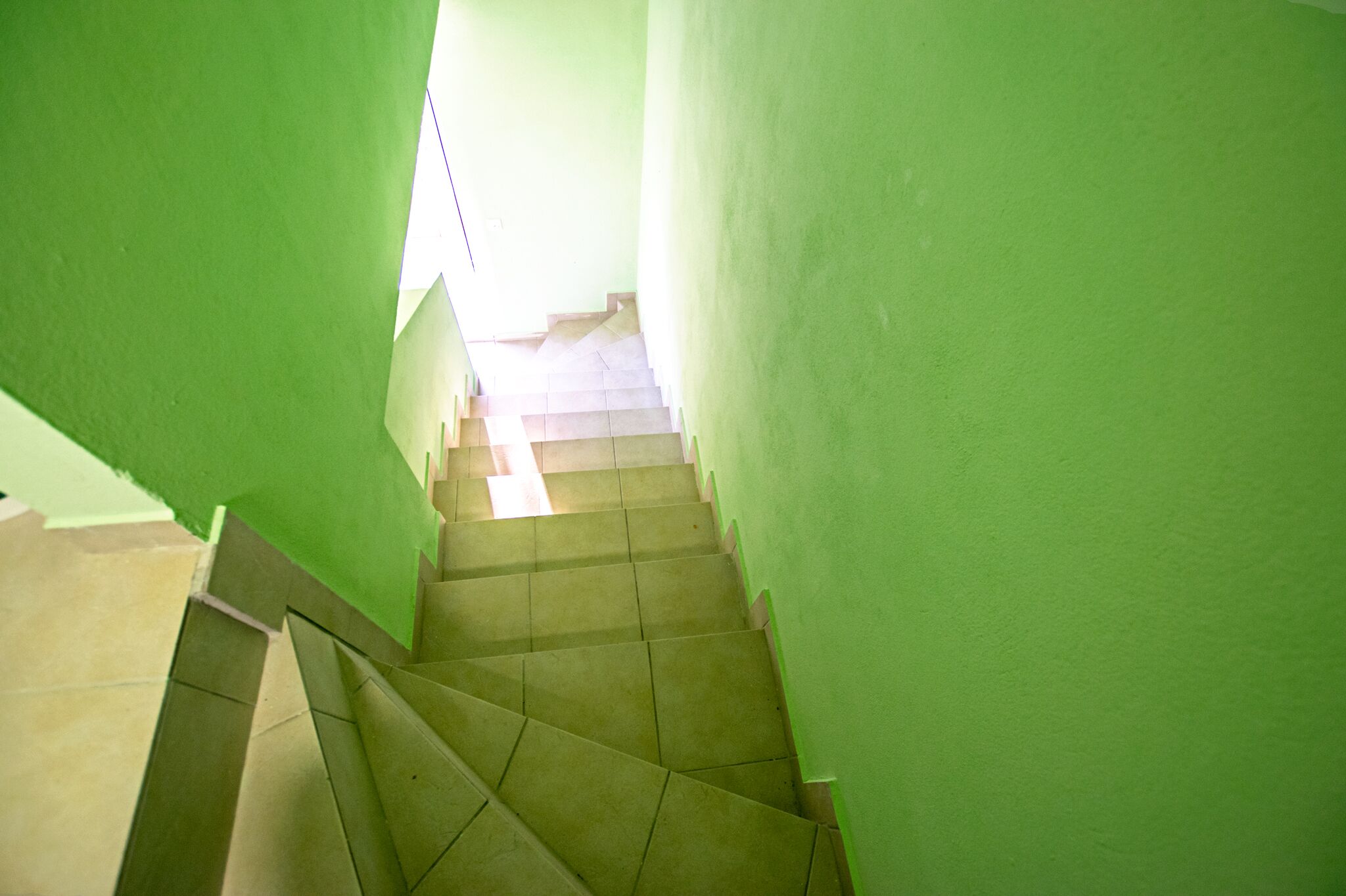 A staircase with green walls and a tiled floor leading to a brighter area at the top.