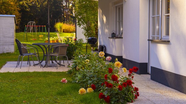Une terrasse avec une table et des chaises, une balançoire et un jardin fleuri.