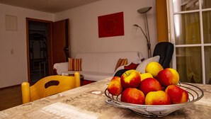 Une table à manger avec un saladier rempli de pommes et de poires, une chaise, un canapé, une lampe et une fenêtre avec des rideaux.