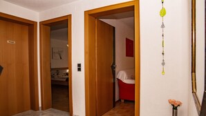 Un couloir d’hôtel avec des portes en bois, un sol en marbre, une salle de bain rouge et un vase rempli de fleurs.