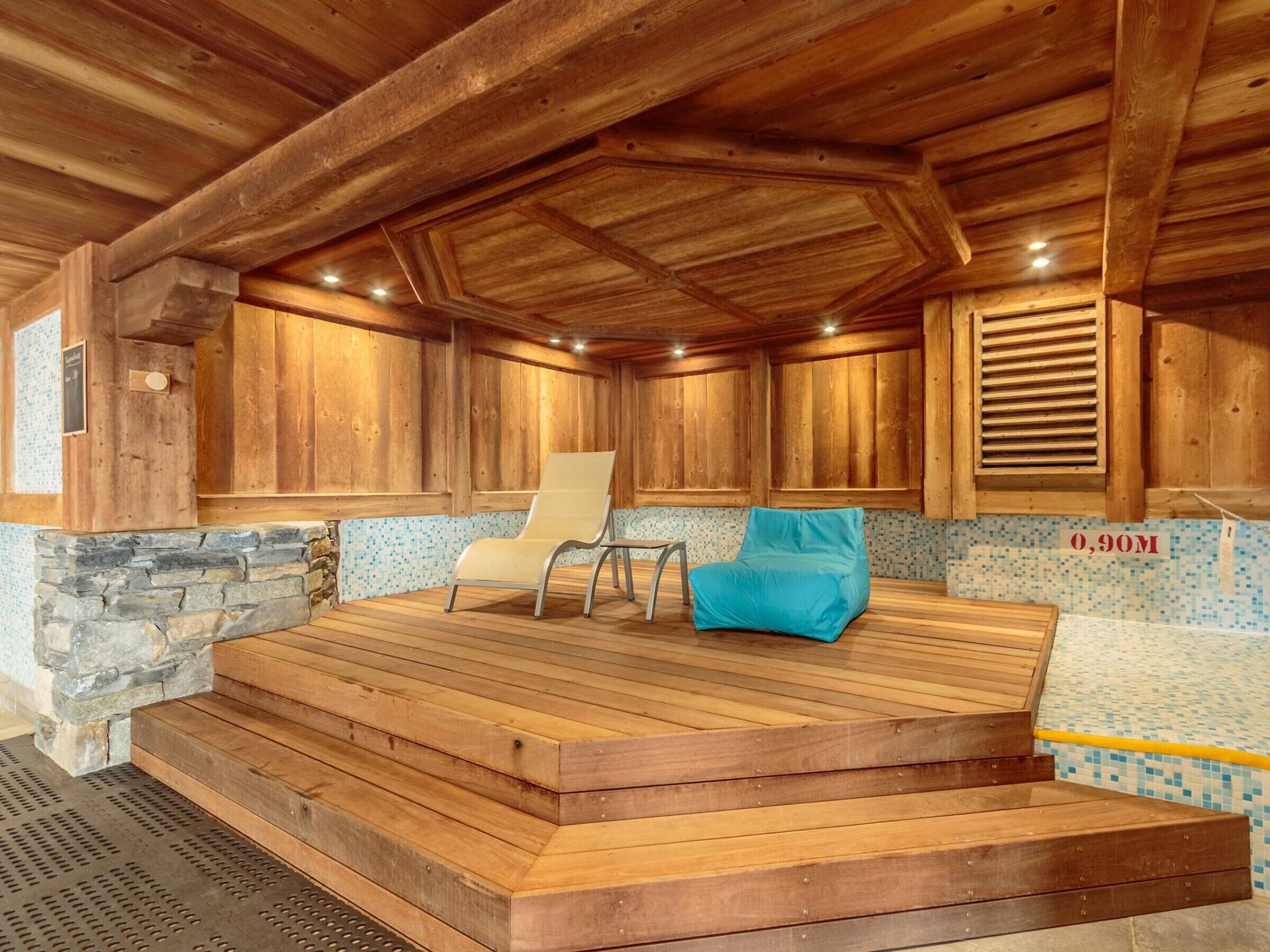 A wooden sauna with a stone wall, a wooden bench, and a blue cushion.