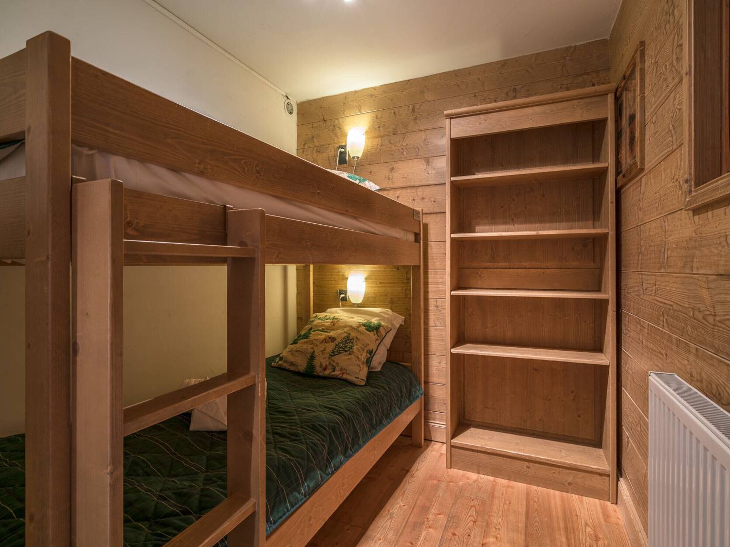 Una camera con un letto a castello in legno, un letto singolo con cuscino decorato e una libreria a muro in legno.