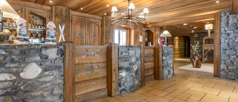 A wooden interior with stone walls, a chandelier, and a bar area with bottles.