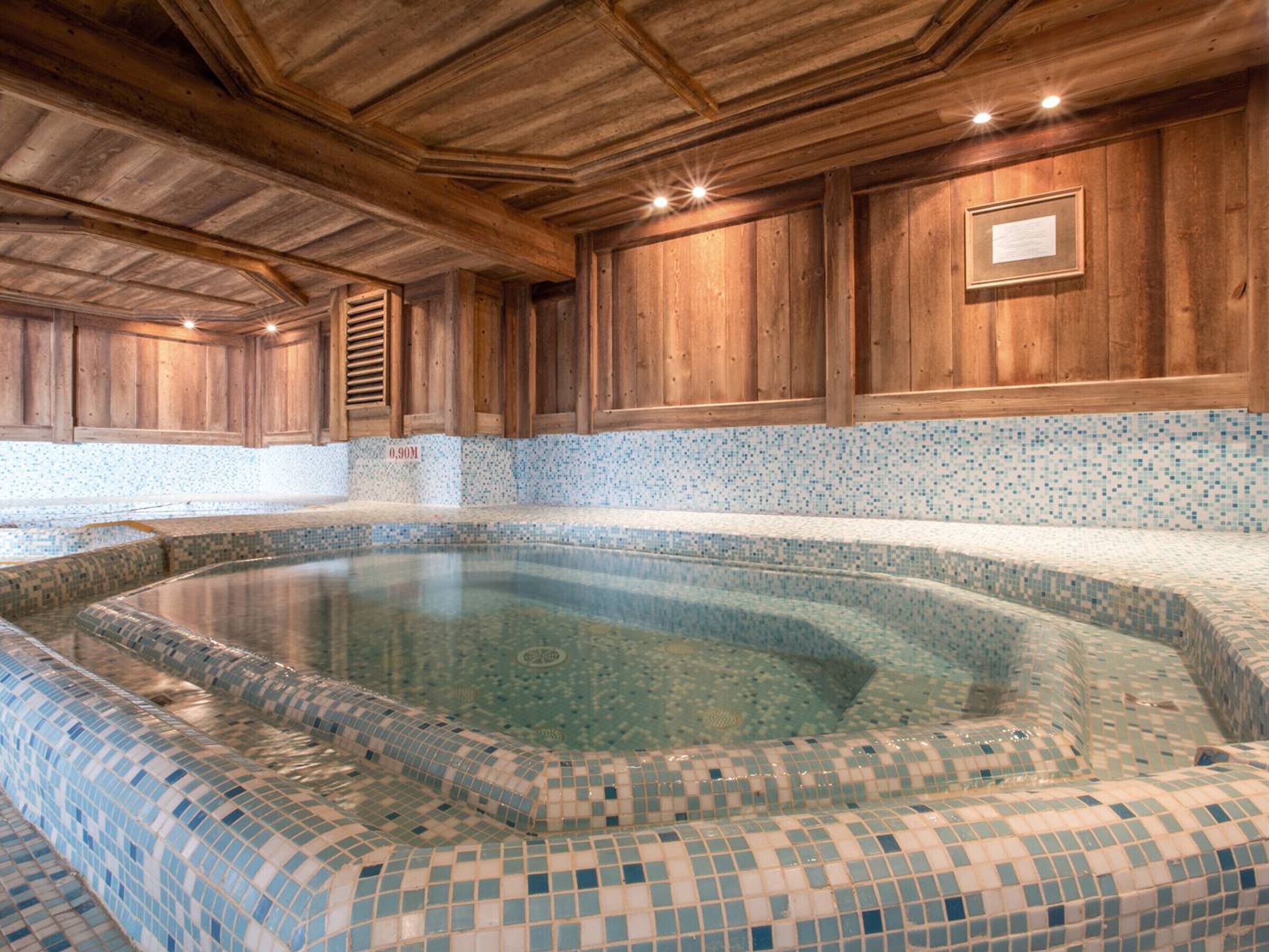 A spa area with a mosaic-tiled hot tub, wooden walls, and a tiled floor.
