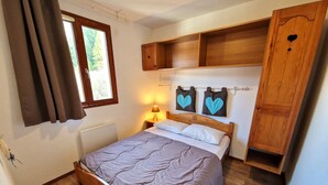 A bedroom with a wooden bed, a nightstand with a lamp, a window with curtains, and a wardrobe with heart-shaped cutouts. - Nice 3-bedroom, 2-bath apartment in Valfréjus, 6/8 people (Valfréjus)