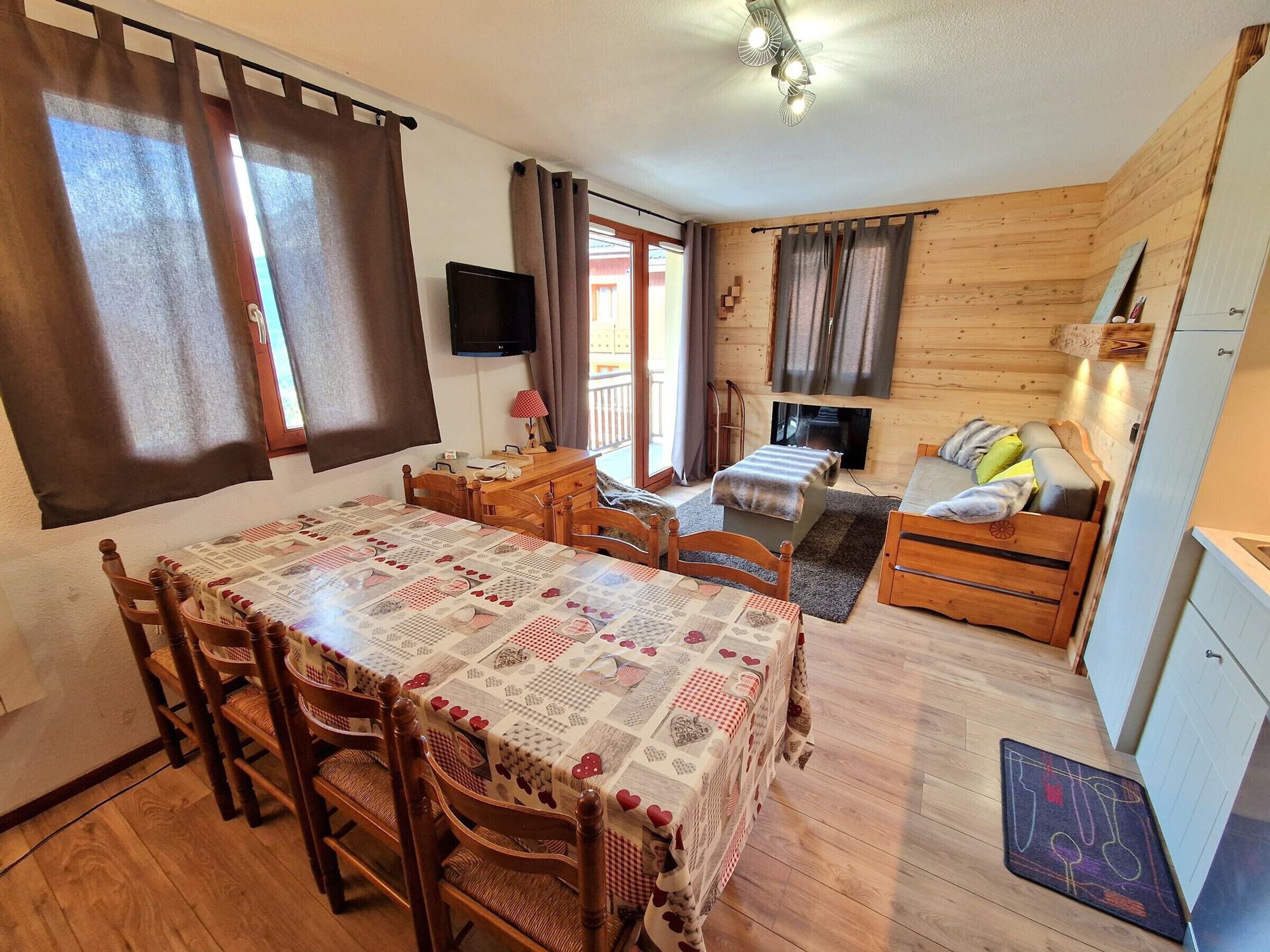 A cozy cabin-style room with a dining table, chairs, a sofa, a TV, and a fireplace.