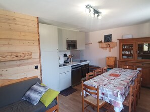 A compact kitchen with white cabinets, a dining table with a checkered tablecloth, and a wooden cabinet with glass doors.