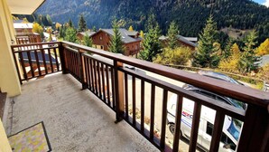 A balcony with a view of a mountain range, houses, and a parked van. - Nice 3-bedroom, 2-bath apartment in Valfréjus, 6/8 people (Valfréjus)