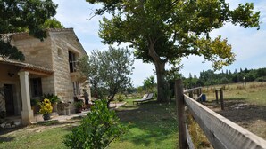 A stone house with a balcony, a grassy yard, and a wooden fence. - Camargue Bed and Breakfast (Le Cailar)