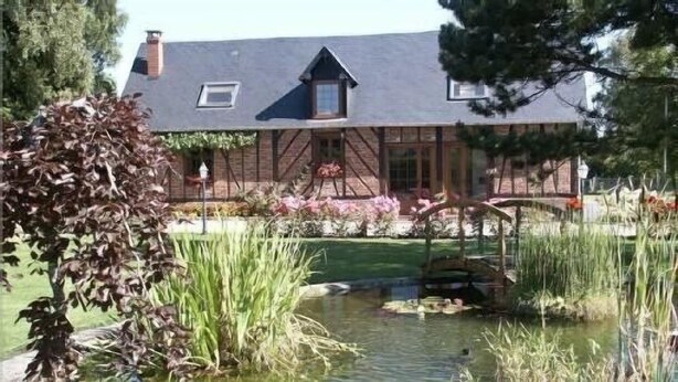 Una casa tradicional con un estanque, rodeada de un jardín lleno de plantas y flores.