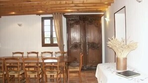 Un comedor con sillas y una mesa de madera, una puerta de madera y un jarrón con plantas secas.