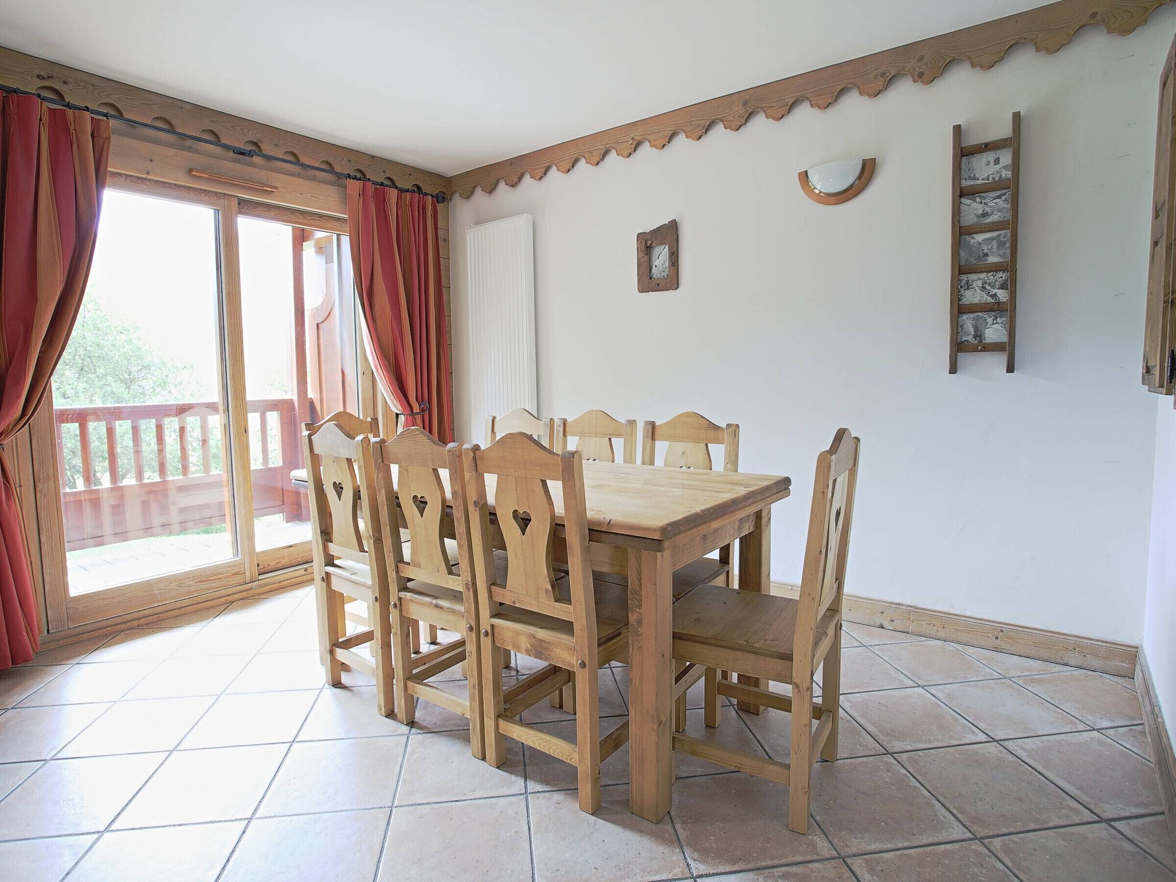 A dining area with a wooden table and chairs, a window with curtains, and a wooden ladder against the wall.