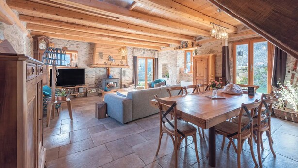 Un interno rustico in legno con camino in pietra, zona pranzo e soggiorno con divano e televisione.