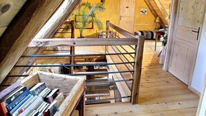 Una stanza mansardata con travi in legno, una scala e vista sul soggiorno sottostante.