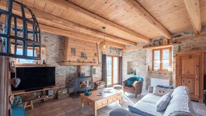 Un soggiorno rustico con parete in pietra, travi in legno a soffitto, televisione, camino e un divano accogliente.