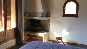 Een slaapkamer met een bed, een stenen openhaard, een raam en een houten plafond.