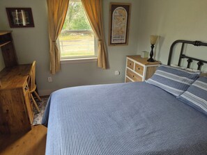 A bedroom with a bed, wooden desk, chair, dresser, and a window with curtains.
