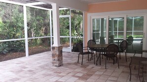 A covered patio with a table and chairs, surrounded by large windows offering a view of greenery. - Luxury, New Home - Serene and Private Vacation Oasis - Minutes from Siesta Key! (Sarasota)