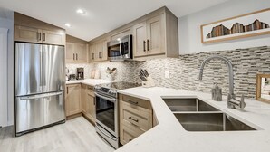 Une cuisine moderne dotée d’appareils électroménagers en acier inoxydable, de meubles en bois et d’un revêtement mural en carreaux.