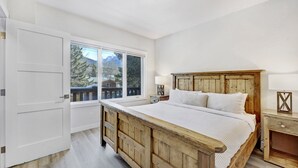 Une chambre à coucher avec un lit en bois, une table de chevet, une lampe et une fenêtre donnant sur des arbres et des montagnes.