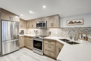 A modern kitchen with stainless steel appliances, wooden cabinets, and a herringbone-patterned backsplash. - Brand New Canmore townhome (Canmore)