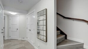 Un couloir avec des portes blanches, un grand miroir encadré et un escalier avec des marches en bois et une rampe en métal.